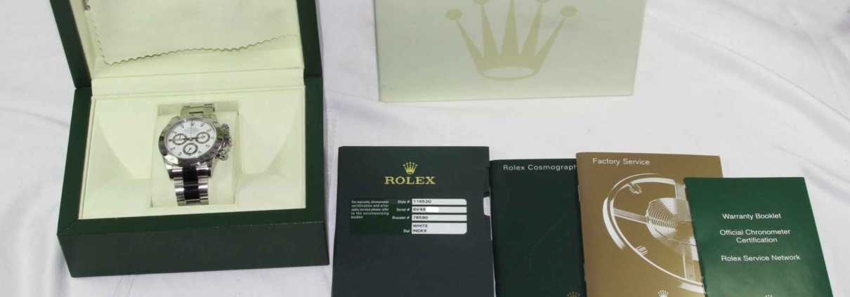 Rolex Daytona watch with original packaging, warranty booklet, and accessories displayed on a white surface.