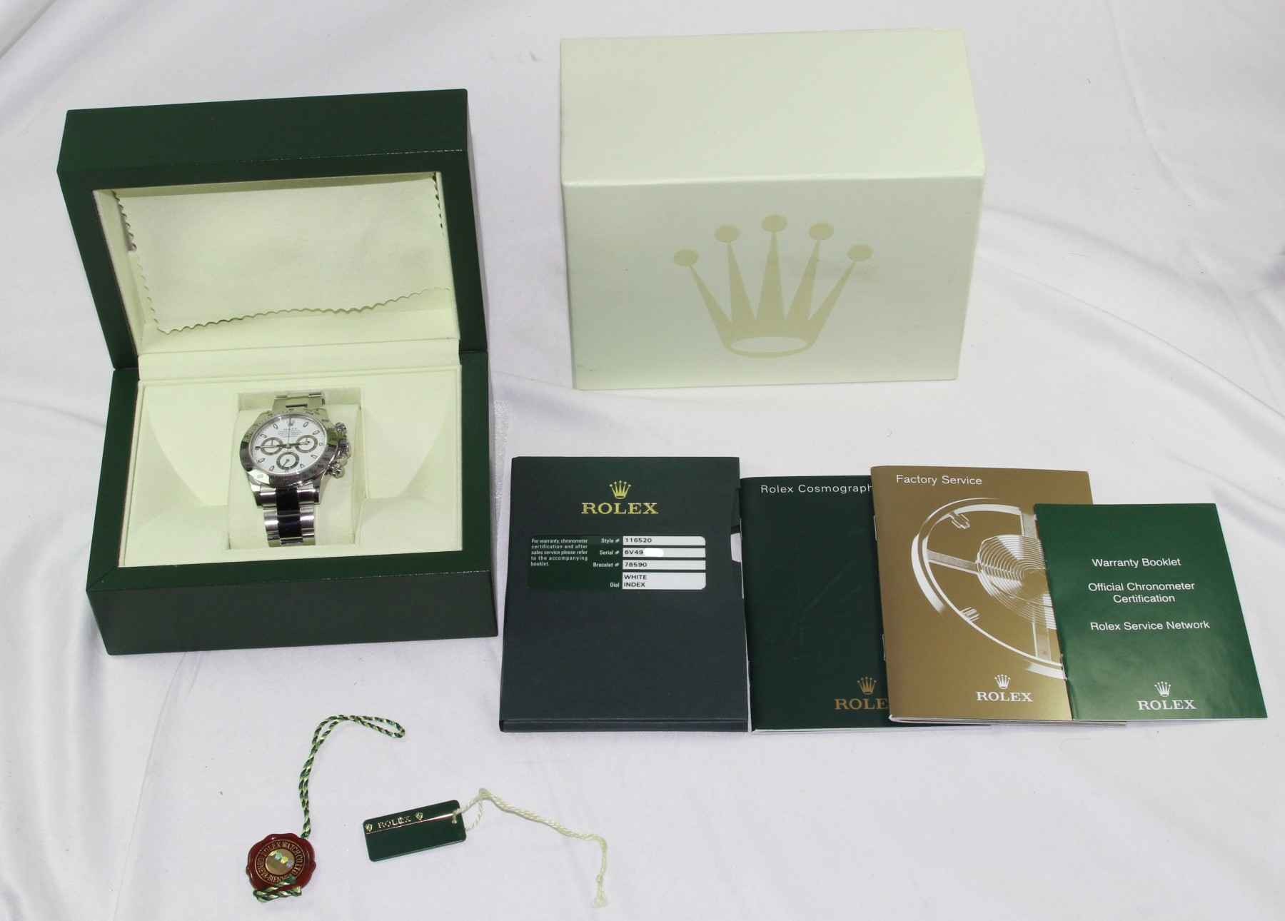 Rolex Daytona watch with original packaging, warranty booklet, and accessories displayed on a white surface.